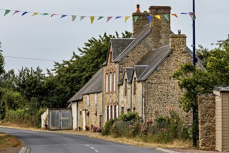A traditional stone house on a rural road with festive garlands, Historic houses in Normandy,