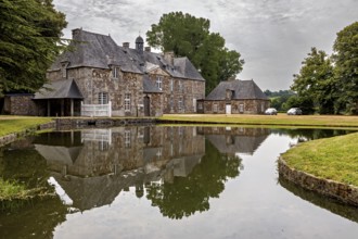 A castle with a pond in front of it, in which the building and the surrounding trees are reflected,