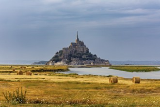A castle island with ecclesiastical architecture in a rural landscape under a cloudy sky, Mont
