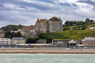 Castle on the coastline with historic buildings and green hills in the background under a cloudy