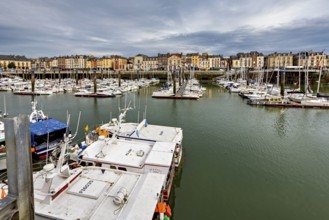 Boats moored in the quiet harbour, surrounded by historic buildings under a cloudy sky, The harbour