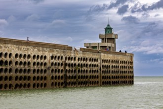 Long harbour wall with lighthouse, surrounded by the sea, under a sky with clouds, The harbour pier