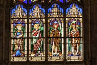 A Gothic church window shows colourful depictions of angels and saints in detailed stained glass,