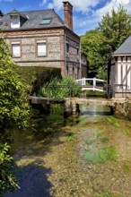 A traditional brick house next to a clear canal with vegetation under a blue sky, The historic mill
