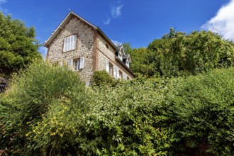 Single brick house behind green bushes and trees under a clear blue sky, The historic mill village