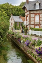 Beautifully landscaped canal with brick houses and flowers, surrounded by natural greenery, The
