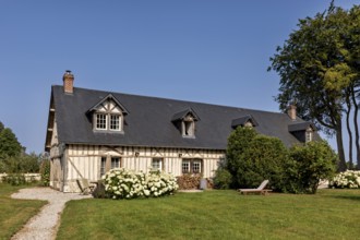 Half-timbered house with a dark roof surrounded by a well-tended garden and flowering shrubs under