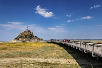 A medieval castle with a long wooden bridge under a clear blue sky, Mont Saint Michel in Normandy,