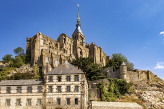Imposing castle and fortress rising against a blue sky, with massive stone walls and towers, Mont
