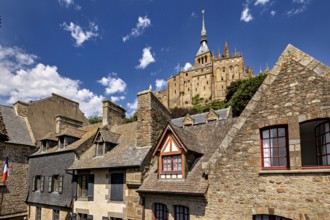 Stone and tiled roofs of ancient buildings with a dominant tower in the background under a clear