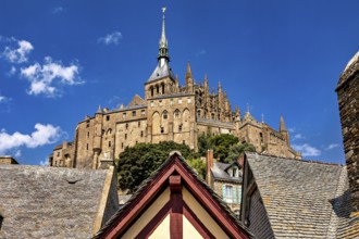 Medieval castle with a towering spire and rooftops against a clear blue sky, Mont Saint Michel in