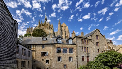 Historic stone architecture with a view of a castle under a blue sky with decorative clouds, Mont