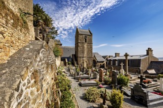 Historic cemetery with church and gravestones along a stone wall under a blue sky with clouds, The