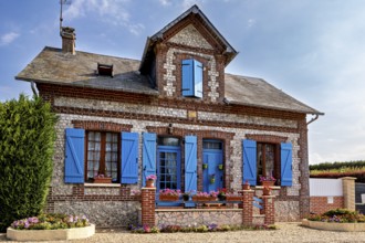 Historic stone house with blue shutters and blooming flowers in decorative plant beds, Historic