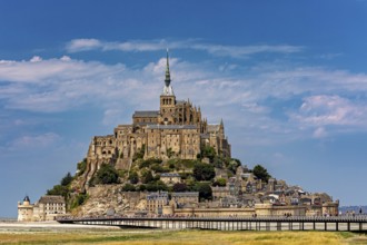 An imposing castle rises against a blue sky with a few clouds, Mont Saint Michel in Normandy,