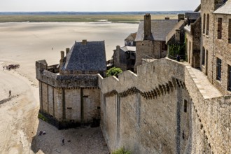 Historic castle wall with a view of a wide expanse of sand and distant buildings under a clear sky,