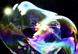 Irregular, iridescent soap bubble in the colours of the rainbow against a black background,