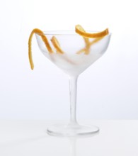 Frosted empty cocktail glass with orange zest as garnish against a white background, studio shot