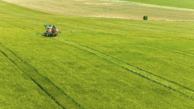Farmer with tractor working in the field. In early summer, he fertilises the grain for an optimum