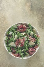 Fresh arugula salad with prosciutto and grated parmesan cheese, on a plate, homemade, no people