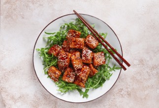 Fried salmon slices, teriyaki with sesame seeds, with arugula salad, top view