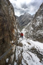 Mountaineer on a rope-secured path in a steep rocky mountain landscape with fresh snow in summer,