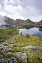 Mountaineer on a rock in front of mountain lakes Wangenitzsee and Kreuzsee, cloudy mountain peaks