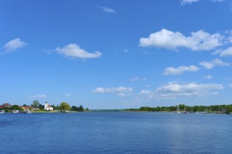 Lake with blue sky and clouds, in the background a village with a church, Rhodes, Etang du Stock,