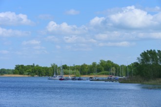 Lake with boats on the shore, surrounded by trees under a blue sky, Rhodes, Etang du Stock,
