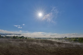 The sun shines brightly over a misty landscape stretching across wide fields, Mönchberg,