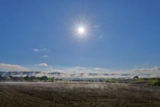 Under a clear sky, the sun shines over a misty, wide landscape, Mönchberg, Miltenberg, Spessart,