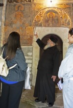 Greek Orthodox priest explains wall paintings from 1802 to visitors, Agia Marina church, Kissos,