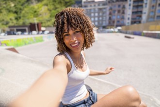 Smiling young woman with curly hair enjoying a sunny day at a skate park while taking a selfie