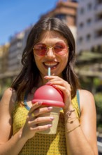 Happy young woman wearing stylish sunglasses, savoring a refreshing iced drink while enjoying a