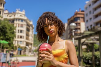 Fashionable young woman enjoys a cold beverage in a vibrant urban setting, embracing the summer
