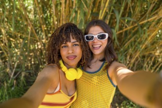 Two smiling girls taking a selfie in front of bamboo plants, wearing yellow clothes and headphones