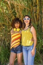 Two female friends hugging and smiling in a vibrant bamboo forest, soaking up the sun and enjoying