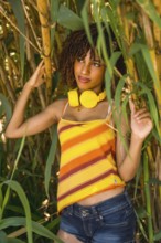 Young woman with curly hair, wearing vibrant yellow headphones, immersing in music while surrounded