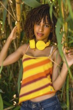 Young woman with yellow headphones enjoying music in a bamboo forest, wearing a colorful striped