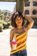 Fashionable young woman enjoying a sunny day in the city, holding a refreshing beverage and