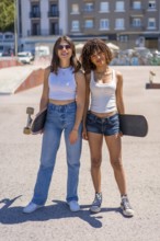 Two young women skaters posing with their skateboards at a vibrant skate park, enjoying the sunny