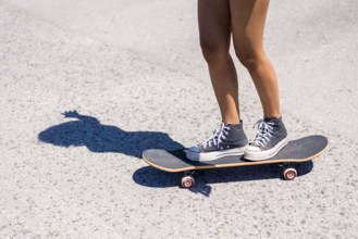 Close up of legs balancing on a skateboard, casting a striking shadow on the asphalt under bright