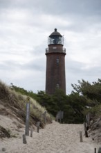 Path through sand dunes leads to the Darßer Ort lighthouse, surrounded by nature and cloudy skies,