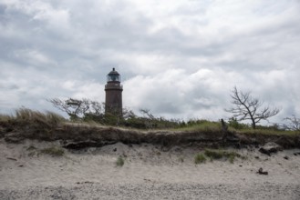 Lighthouse behind sand dune with sparse vegetation and dramatic cloudy sky, Prerow,