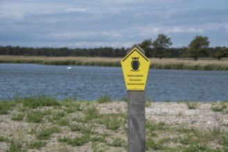 Yellow national park sign with owl in the foreground, water and cloudy sky in the background,