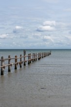 Wooden footbridge leads into the calm, blue sea under a slightly cloudy sky, Prerow,