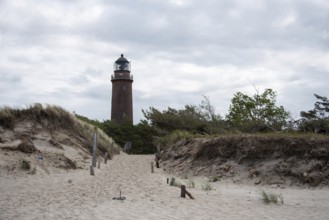 Path through sand dunes leads to the Darßer Ort lighthouse, surrounded by nature and cloudy skies,