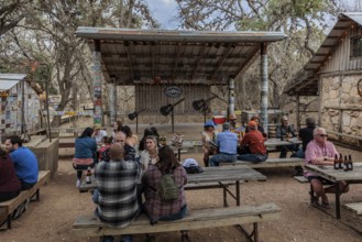 Tourists drinking beer at an open-air bar with a bandstand in Luckenbach, Texas, USA
