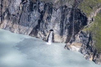 Waterfall cascades from a rock face into a blue mountain lake, Lac des Dix reservoir, Valais Alps,