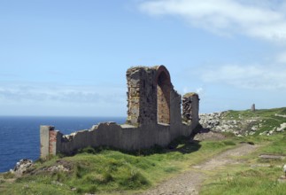 A coastal ruin with a view of the blue sea and green meadows under a cloudy sky, Mining, Botallack,